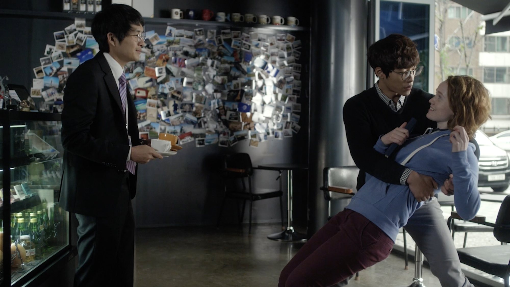 In a cafe, a man in glasses dips Claire backward while a man in a suit holds two coffees