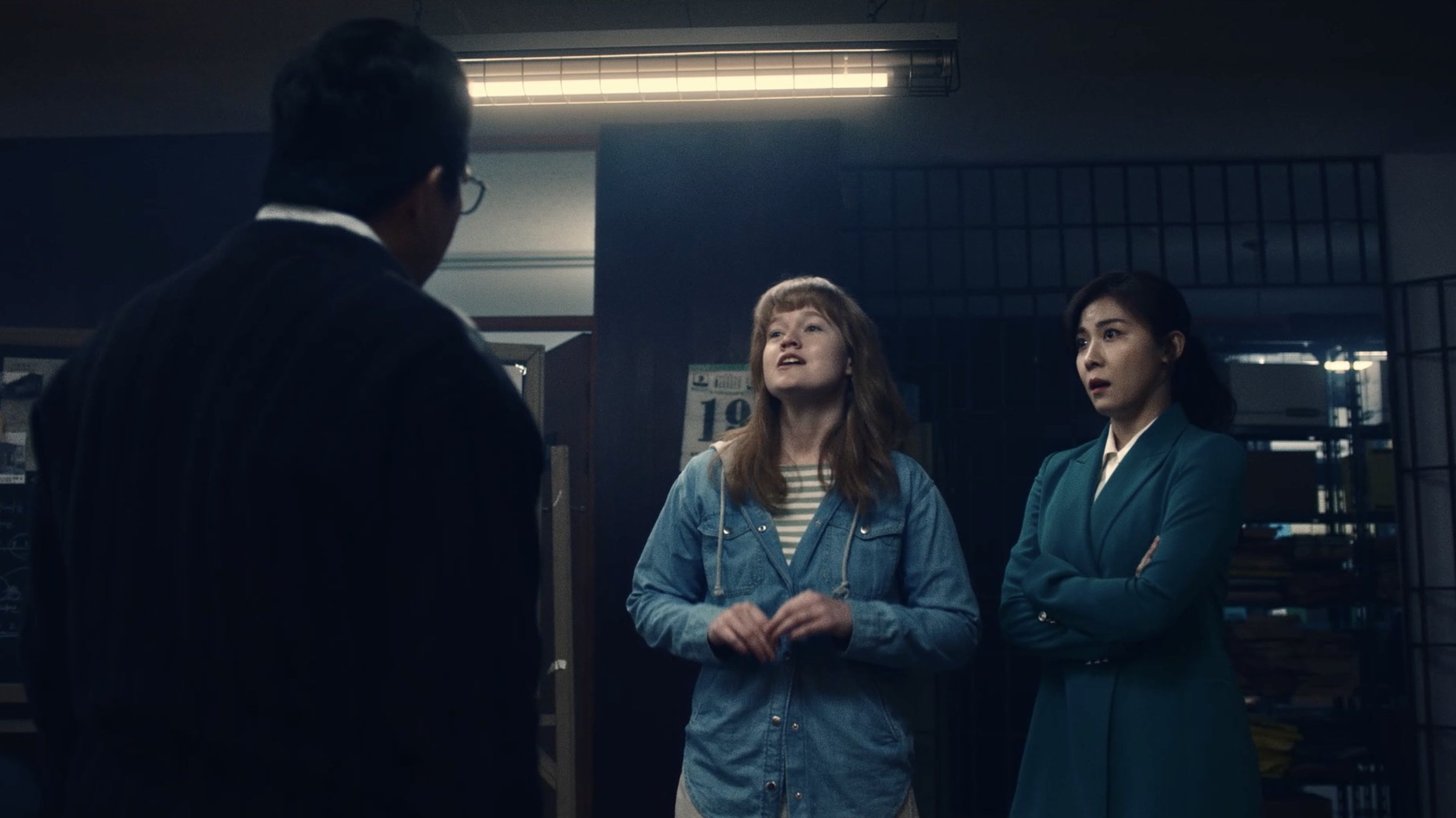 Claire talks fast in a dim 1980s police office as a detective in a teal coat looks on, startled