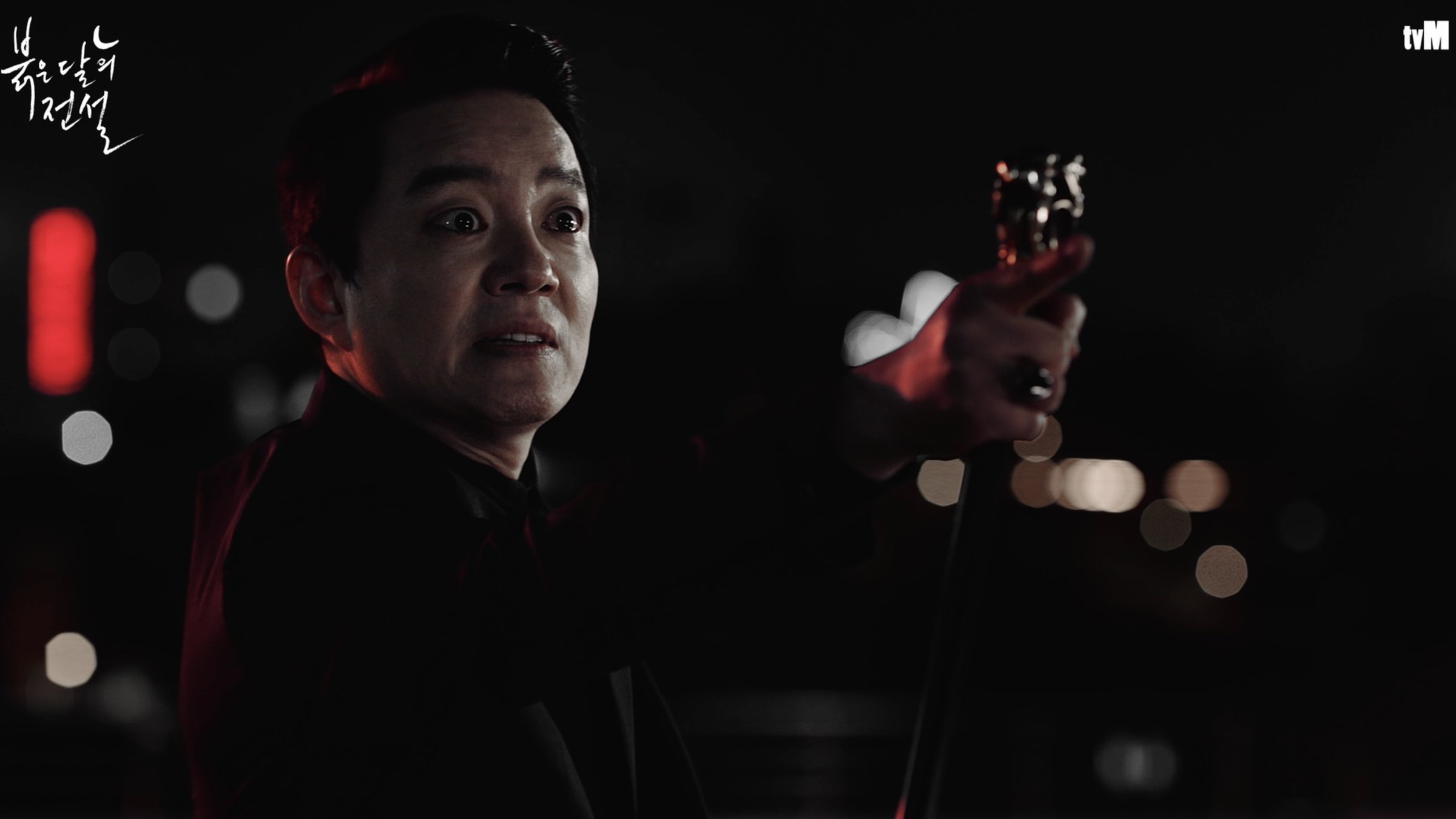 A wide-eyed man holds up an ornate cane at night, in another of the show's in-world K-dramas