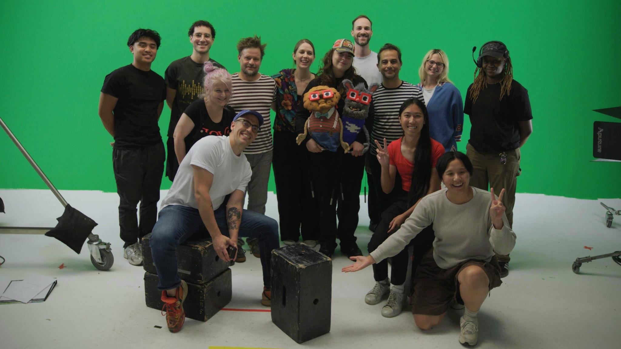 The We're From The Internet cast and crew on the green-screen stage, holding up the Chip and Benny puppets